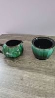 Sugar bowl and creamer side by side showing green drip glaze, black interiors and brown rims
