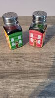 Front view of the salt and pepper shakers showing green and red painted house sides with windows and doors.