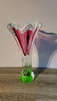 Front view of the tall tulip style crystal glass vase showing the pink center, white highlights, and green base against a plain background on a wooden surface.