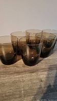 Six light brown lowball glasses arranged in 2 rows of 3 on a wooden surface.