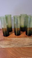 Photo showing all five deep green highball glasses arranged upright on a wooden surface.