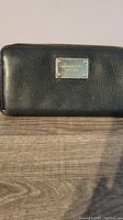Front view of the black Michael Kors wallet showing the silver logo plate and zipper design.