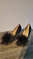 Right side view of black satin high heel pumps with large feather detail at toe.