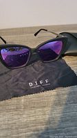 Large DIFF sunglasses with reflective blueish pink tint lenses on DIFF cleaning cloth and black case.