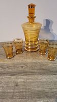 Full view of amber colored vintage decanter and four matching glasses arranged on a wood surface showing size and design.