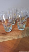 Four vintage etched glasses arranged on wooden surface, showing clear glass with multicolor leaf designs