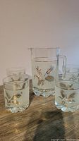 Photo showing the pitcher and four matching lowball glasses with etched gold leaf designs on frosted glass.