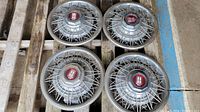 Four 14 inch metal wire spoke style hubcaps with red emblem centers shown stacked on a wooden pallet.