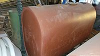 Side view of large reddish-brown cylindrical oil tank with legs, showing size and shape of the tank.