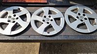 Top view showing the front of three silver-colored Toyota plastic wheel covers with 5-spoke design and visible scratches.