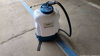 Front view of the white and blue Sanipro Sanisprayer 360 electric backpack sprayer on pavement, showing its tank and attached hose.