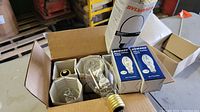 Box containing several unused light bulbs including Sylvania Metalarc and boxed Howard Metal Halide bulbs.