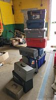 Stacked tool boxes in a workshop environment showing varied sizes and brands including Craftsman and Coleman.