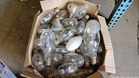Box filled with approximately 25 used large industrial light bulbs of various shapes and types.