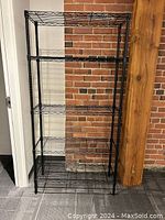 Front view of the black metal wire shelving unit standing against a brick wall.