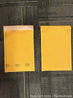 Two bubble mailer envelopes, one showing the peel and stick flap open, other showing sealed front side on carpeted floor.