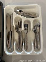 White plastic cutlery tray filled with stainless steel cutlery - including knives, forks, large spoons, and small spoons.