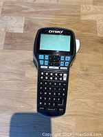 Photo shows one black handheld Dymo label maker with blue buttons and QWERTY keypad, no power cord visible.