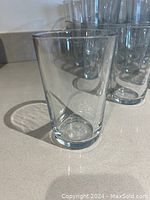 Side view of one clear IKEA glass tumbler in front of the assembled set of glasses on a smooth countertop.