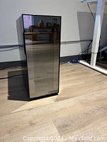 Black Koolatron wine fridge with a mirrored door standing on wooden floor, closed.
