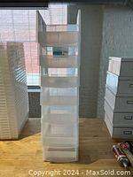 Seven transparent plastic stacking bins stacked vertically on a table.
