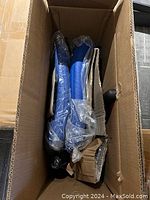 Box containing unassembled chair parts wrapped in plastic including blue leatherette cushions and chair bases.