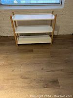 Front view of the white metal shelf unit with wooden poles, showing three shelves and overall structure.