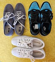 Top view of three pairs of women's shoes: Nike Flyknit runners in black and blue, grey suede Keds, and white Tretorn sneakers