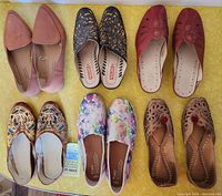 Top-down view of six pairs of women's shoes arranged on yellow surface showing all shoe pairs: tan George slip-ons, black and red Pikolinos sandals, colorful Toms slip-ons, leather Egyptian and Moroccan style slip-ons.