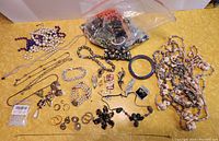 Overview photo showing assorted costume jewelry items including necklaces, earrings, brooches, and loose beads in a bag