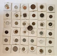 Top view of approximately 40 foreign coins each in individual white paper sleeves with transparent windows, laid flat in a grid pattern.