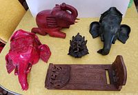 Top view showing the arrangement of all five items including the large red ceramic elephant container with separate lid, greenish-black elephant head planter, small metal elephant figurine, carved wooden expanding book holder and red ceramic elephant head planter.