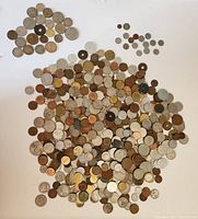 Many coins scattered on white background showing variety of metals, sizes, and designs.