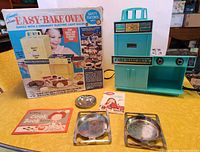 Complete lot laid out on table showing Easy-Bake Oven in original box, oven unit, metal pans, mold, and booklets