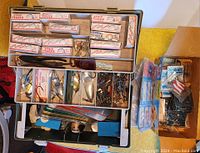 Overhead view of large fishing tackle box showing multiple compartments packed with vintage lure boxes and loose fishing tackle including hooks, flashers, and other accessories