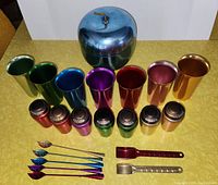 Front view of lot showing all items arranged with ice bucket at center back, colorful glasses and spice containers in rows, stir sticks and measuring spoons in front
