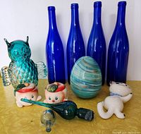 Full lot display including teal glass owl, four blue bottles, tomato salt & pepper shakers, glass egg, kitten wall pocket, and two glass stoppers.