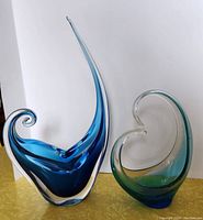 Side view of tall blue glass sculpture with clear accents next to shorter green-blue swirl glass piece