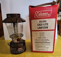 Photo of the vintage Coleman lantern next to its original red box labeled Deluxe Easi-Lite Lantern.