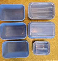 Overhead view of six light blue Delphite fridge dishes, three with clear ribbed lids and three without lids.