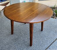 Front view of the round wood dropleaf table with both leaves open, showing the smooth surface and wood grain.