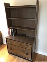 Front view of wooden bedroom bureau with attached bookcase. Shows three shelves above a bureau surface with two drawers below, the bottom drawer featuring decorative metal latches.