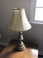 Pair of brass side lamps with tiered bases and decorative white and gold swirl shades on a wooden table near window.
