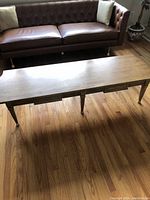 Solid wood rectangular coffee table next to a brown leather sofa, showing side view and leg detail.