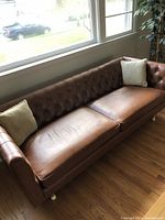 Brown vinyl couch from side angle showing tufted back and one accent pillow