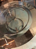 Top down and angled view of the round glass table showing the clear glass surface, silver metal frame with mirror finish, circular metal support ring, and polished legs.