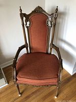 Full view of the high back chair upholstered in red fabric with ornate dark wood carvings and finials.