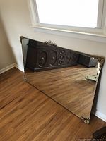 Front angled view of the large rectangular mirror leaning against a wall, showing reflective glass surface and decorative metal corners.