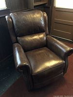 Brown vinyl lounge chair with cushioned back and armrests, showing overall condition and details such as studded trim.
