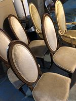 Photo of six dining chairs arranged in a cluster, showing two chairs with armrests and four armless chairs with beige upholstery and dark wooden frames.